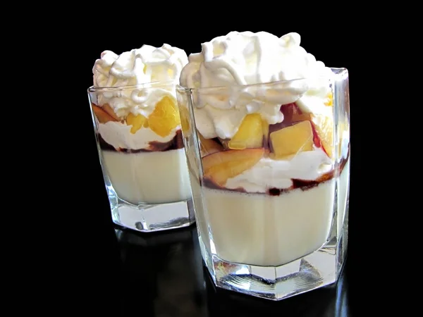 Two glasses with panna cotta dessert with peaches, whipped cream and meringue