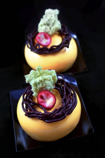 Orange mousse desserts with chocolate nest decoration, cranberry and pistachio sponge