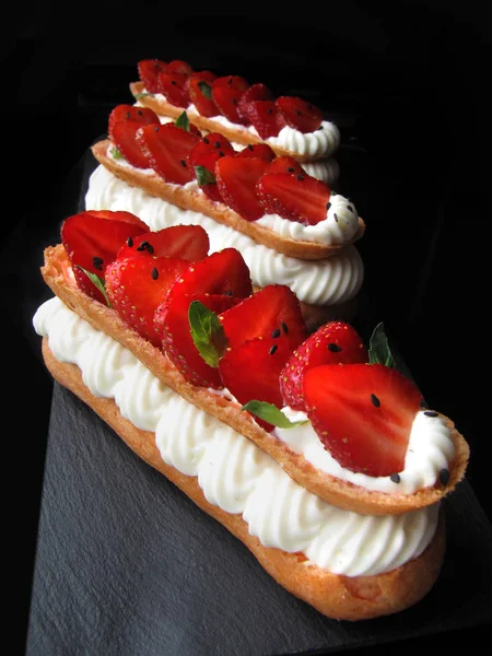 Fresas y eclairs de crema con bayas frescas y hojas de menta sobre fondo negro — Foto de Stock