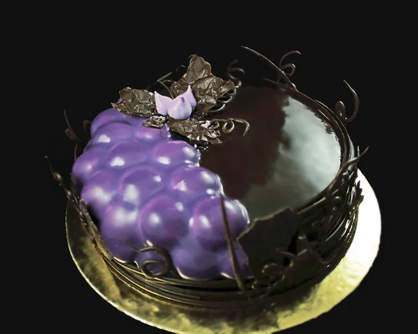 Purple grapes and chocolate cake decorated with chocolate vines border on golden coaster