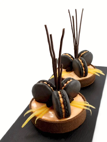 Orange chocolate tarts with black french macarons and persimmon on white background