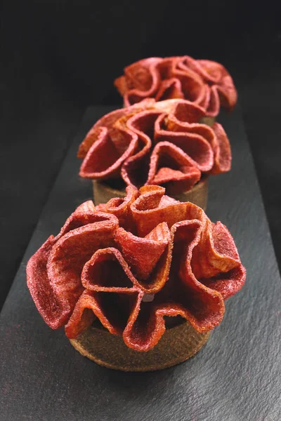 Red fruit leather ruffled dessert tarts on black background