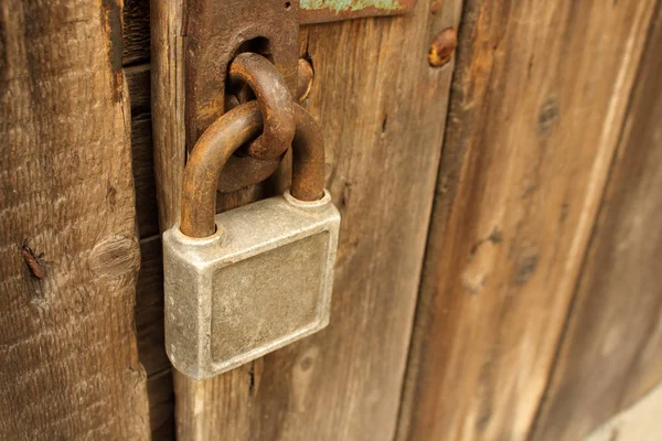 Antiguo candado de escuadra oxidada colgando de la puerta de madera marrón —  Fotos de Stock