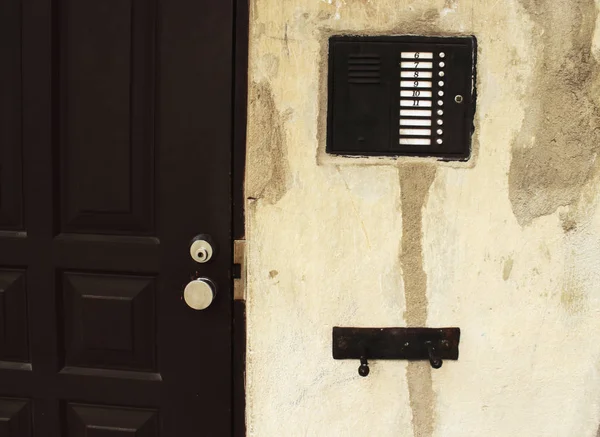 Dispositivo de intercomunicação com números na parede de gesso quebrando velho perto da porta de entrada preta — Fotografia de Stock