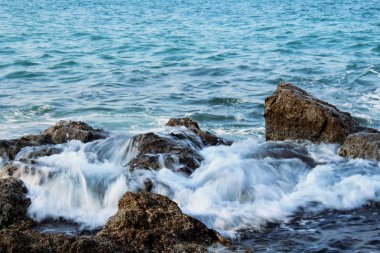 Mavi su arka plan üzerinde ıslak deniz kayaları üzerinde akan köpüklü deniz dalgaları