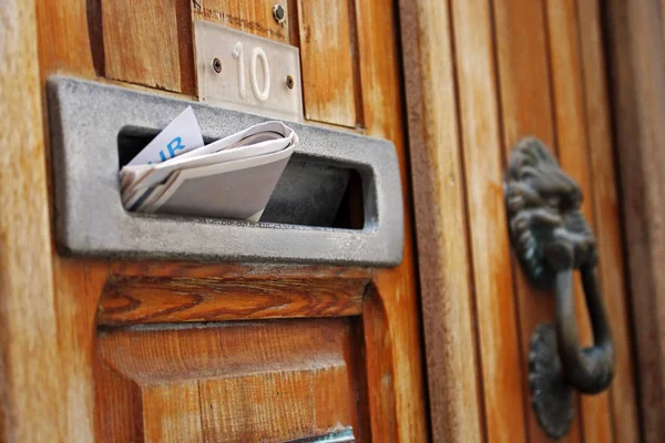 Mail box filled with rolled spam newspaper in old wooden door