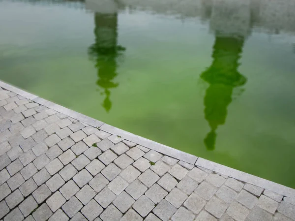 Πράσινο νερό λίμνη κατά μήκος πλακόστρωτου δρόμου με αντανακλάσεις — Φωτογραφία Αρχείου
