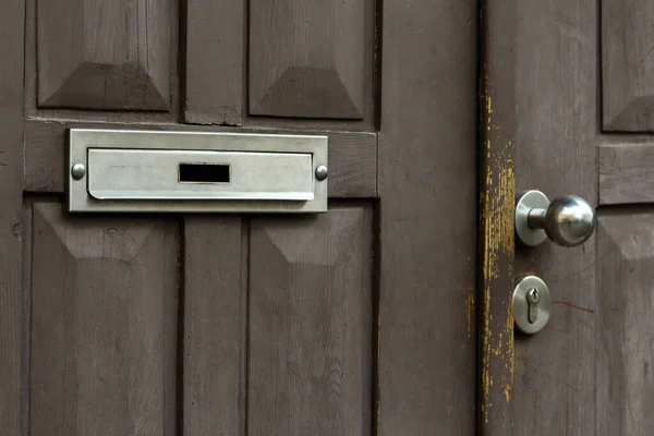 Grey wooden door with empty mailbox hole and visible door handle bokeh