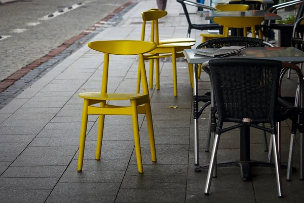 湿った舗装の上に立つさまざまな黄色と黒の通りのカフェチェア — ストック写真