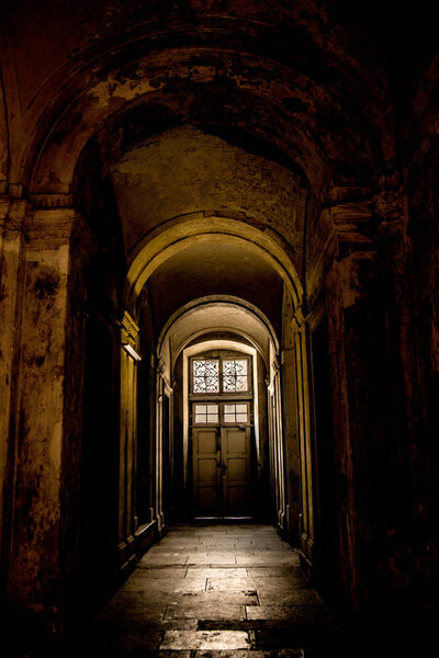 A gloomy corridor with a door at the end, from which comes the light.