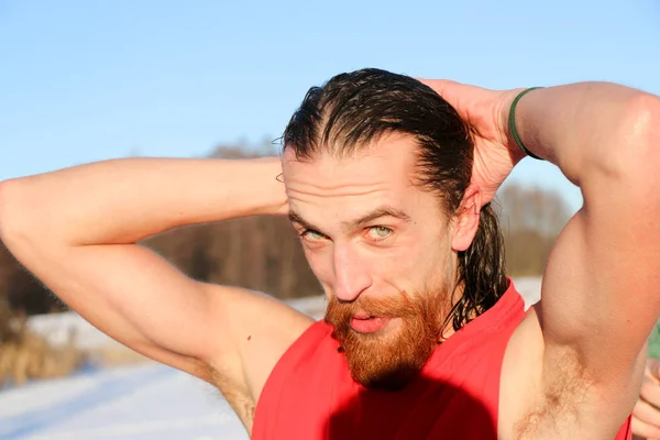 Young Good Looking And Attractive Man With Muscular Body, with a red beard and long hair Wet Taking after taking an ice bath. handsome attractive men showering next to swimming pool. water drops are falling on his torso. Sunny winter day in Ukraine,