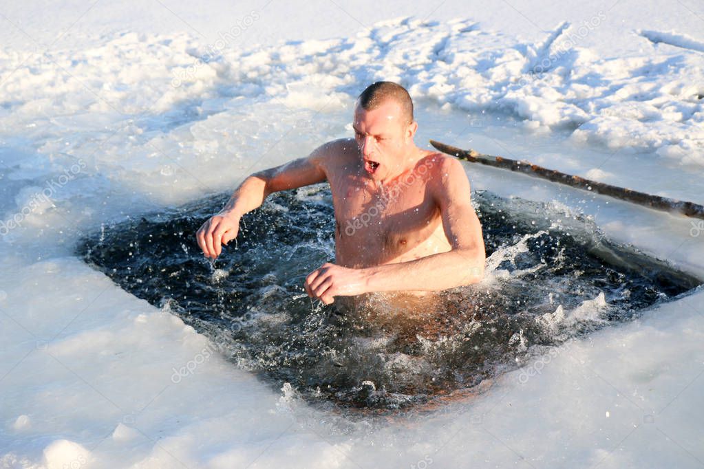 A young, slim, handsome, strong, athletic man, naked, diving into the icy water in the winter, against a snowy landscape, a bright sunny day, many beautiful drops and splashes. Ukraine, Shostka