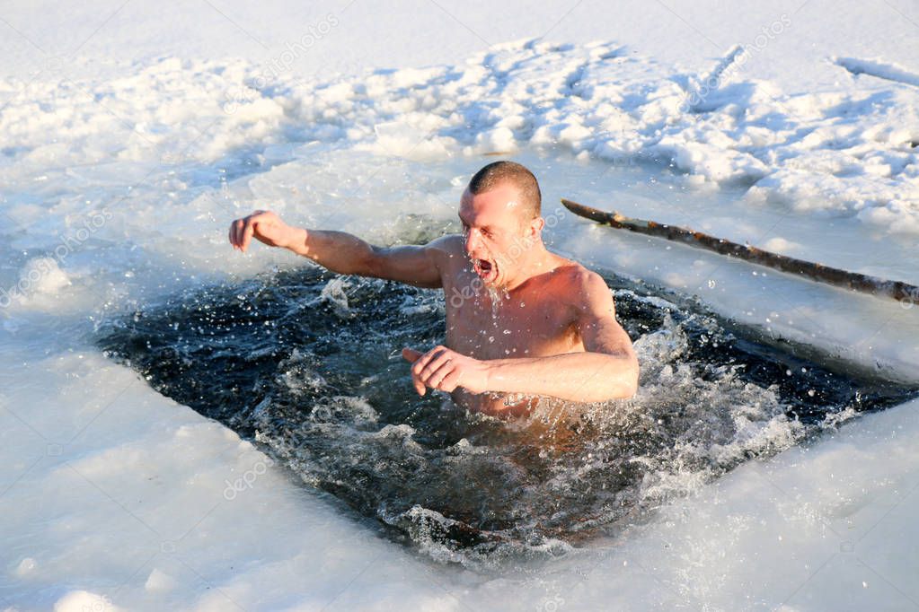 A young, slim, handsome, strong, athletic man, naked, diving into the icy water in the winter, against a snowy landscape, a bright sunny day, many beautiful drops and splashes. Ukraine, Shostka