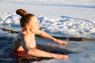 Güzel bir genç kız, Kızıl saçlı, bir yan-parça mayo güzel güneşli bir günde gölde Kışın buzlu suya dalıyor. Ukrayna,: Sumy Oblast, Shostka