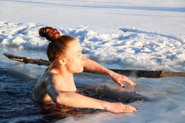 Güzel bir genç kız, Kızıl saçlı, bir yan-parça mayo güzel güneşli bir günde gölde Kışın buzlu suya dalıyor. Ukrayna,: Sumy Oblast, Shostka