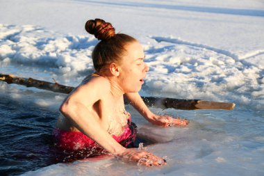 Güzel bir genç kız, Kızıl saçlı, bir yan-parça mayo güzel güneşli bir günde gölde Kışın buzlu suya dalıyor. Ukrayna,: Sumy Oblast, Shostka