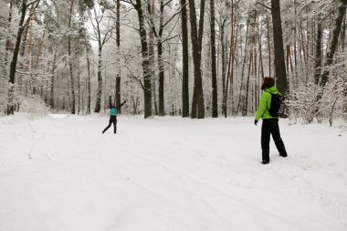 Güzel mutlu çift kar topu atıyor ve kış parkında eğleniyor. İnsanlar kışın ormanda yürürler. Bir sürü kar, muhteşem doğa. Erkek ve kız. Genç çift, doğada yürür. Dostlar güzel çam ormanının tadını çıkarın..