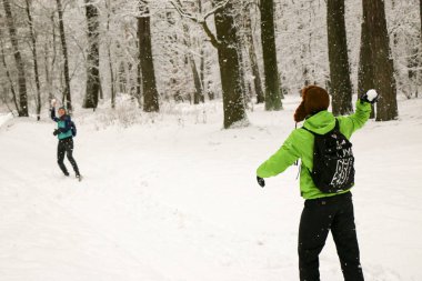 Güzel mutlu çift kar topu atıyor ve kış parkında eğleniyor. İnsanlar kışın ormanda yürürler. Bir sürü kar, muhteşem doğa. Erkek ve kız. Genç çift, doğada yürür. Dostlar güzel çam ormanının tadını çıkarın..