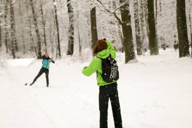 Güzel mutlu çift kar topu atıyor ve kış parkında eğleniyor. İnsanlar kışın ormanda yürürler. Bir sürü kar, muhteşem doğa. Erkek ve kız. Genç çift, doğada yürür. Dostlar güzel çam ormanının tadını çıkarın..