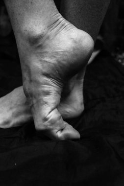 Kadın bacakları, eller. Güzel ayaklar ve avuçlar siyah arka planda, yakın plan. Siyah beyaz fotoğraf, doğal ışık..