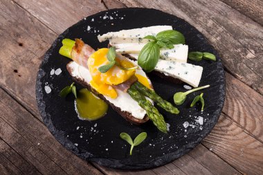 Izgara yeşil kuşkonmaz pastırma, haşlanmış yumurta, Brüksel lahanası ve mavi peynir üzerinde siyah taş Kayrak ile üzerinde eski ahşap rustik arka plan üzerinde sarılı sopa ile tost.