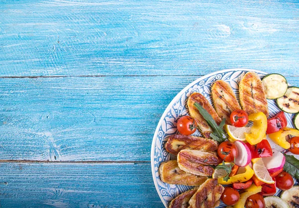 Set collection of cheese and snacks. Grilled halloumi, pepper, zuccini, tomato cherry and radish over on blue wooden  background. Overhead. Copy space.