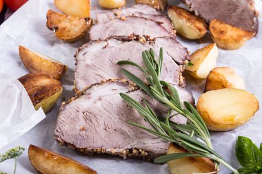 Fırında patates, soğuk haşlanmış domuz eti, biberiye ve beyaz parşömen üzerine üzerinde fesleğen. Üstten görünüm.