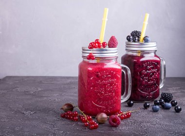 Ahududu, kırmızı ve siyah frenk üzümü, goosberries, yaban mersini, böğürtlen içinde gri beton zemin üzerine gözlük, yaz smoothies. Sağlıklı beslenme diyet vejetaryen kavramı.