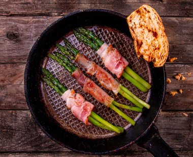 Domuz pastırmasına sarılı kızarmış yeşil kuşkonmaz ve ahşap arka planda kurutulmuş domatesli ev yapımı ekmek. Üst Manzara. Boşluğu kopyala