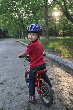 Küçük beyaz bir yürümeye başlayan çocuk koruyucu bir kaskı kafasına takıyor bir bebek bisiklete biniyor. İki tekerlekli kırmızı bisiklet üzerinde yürümeye başlayan çocuk.