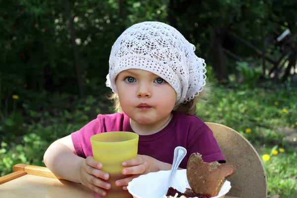 A cute little girl having breakfast is holding a yellow glass with a drink. Breakfast in the fresh air, we instill the skills of early self-care in childhood.