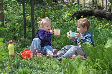 Küçük çocuk ve kız çimenlerin üzerinde otururken içki içiyorlar.