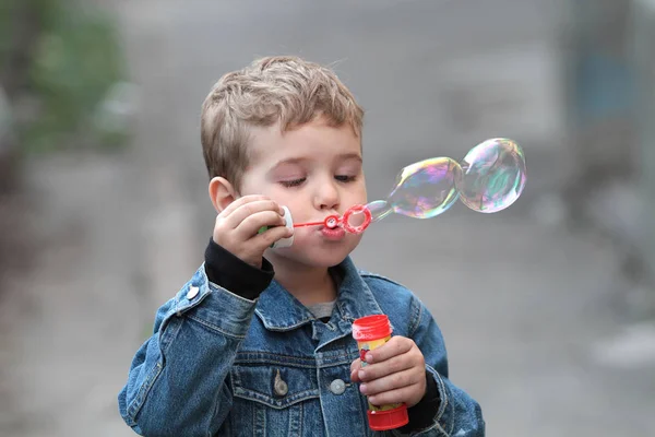 The boy in the denim jacket blows bubbles — Stock Photo, Image