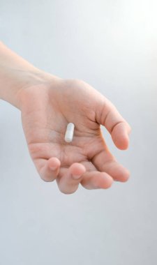 Kapsül şeklinde beyaz-gri bir hap uzanmış bir dişinin elinde yatıyor.