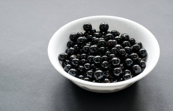 Fresh black currant on a snow-white plate, which stands on a black background. Side view