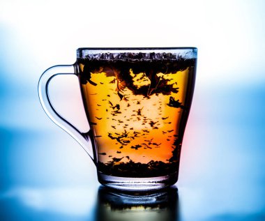 Bir cam bardak bitkisel çay demlendi. Yüksek karşıtlık. Doygun renklere. Beyaz ışık ve kenarlarında mavi arka plan. Yakın çekim.