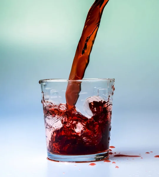 Bir cam kabı kırmızı vişne suyu akışı ile dolu. Beyaz ve turkuaz arka planını renklendirin. Yüksek karşıtlık. Doygun renk.