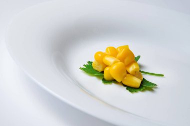 Beyaz bir tabakta maydanoz yaprağına bir avuç konserve mısır. Yan görünüm.