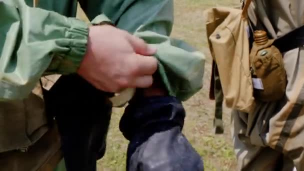 A young soldier in a military department puts on rubber gloves of a combined-arms protective kit. A cadet on his belt stands next to a flask and a military tablet — Stock Video