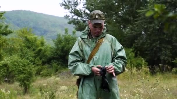 Vojenský kadet voják v ochranném obleku se pokouší nosit rukavice během deště v Černobylském lese. V uniformě, která to udělala. Nebezpečí radiace — Stock video