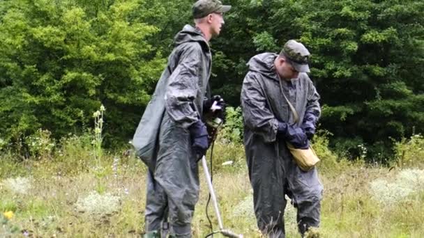 Deux cadets militaires sur un site forestier de Tchernobyl sont à la recherche de mines avec un détecteur de mines sous la pluie. Protégé dans une combinaison contre les radiations. Le gars essaie d'obtenir de l'équipement du sac — Video