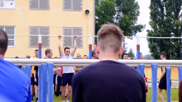 Athletic Guy drar sig på en horisontell bar i ett militärt läger för att få en tillfredsställande rating med andra tittare — Stockvideo