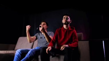 Zaferin tadını çıkarıyorum. Duygusal iki genç adam kanepede oturup oyun konsolu oynayıp, elinde joystick tutarak heyecanlılar. Kablosuz kontrolörle oyun oynayan erkekler. Samimi oda