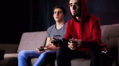 Zaferin tadını çıkarıyorum. Duygusal iki genç adam kanepede oturup oyun konsolu oynayıp, elinde joystick tutarak heyecanlılar. Kablosuz kontrolörle oyun oynayan erkekler. Samimi oda