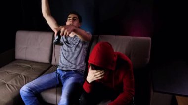 Zaferin tadını çıkarıyorum. Duygusal iki genç adam kanepede oturup oyun konsolu oynayıp, elinde joystick tutarak heyecanlılar. Kablosuz kontrolörle oyun oynayan erkekler. Samimi oda