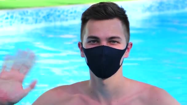 Homme blanc caucasien agitant la main dans la piscine dans un masque médical protecteur pour protéger. Concept de l'impact de l'épidémie de coronavirus sur une industrie du voyage pour la saison estivale 2020, isolement par confinement. — Video