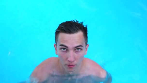 Porträtt av en man dyker under vatten från poolen titta på kameran. Ung kille under vattnet simmar i kristallklart blått vatten. Begreppet sport, simbassäng, konkurrens, fitness. Stockfilm