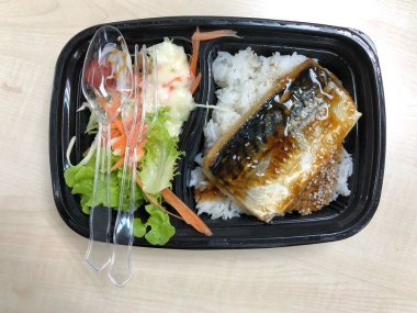 Plastik kaptaki pirinç kasesinin üstünde teriyaki sosuyla kızartılmış Saba balığı.