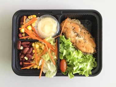 Masadaki yemek kabında salata ile ızgara somon balığı. 