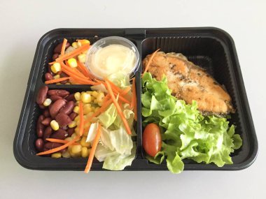 Masadaki yemek kabında salata ile ızgara somon balığı. 